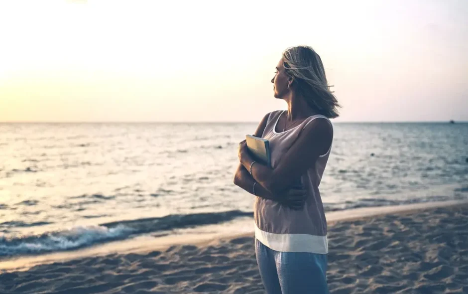Woman in jeans and jumper staring out at the ocean at sunset