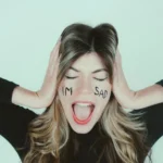 Woman acting as drama queen with hands over ears and words I'm Sad on her face