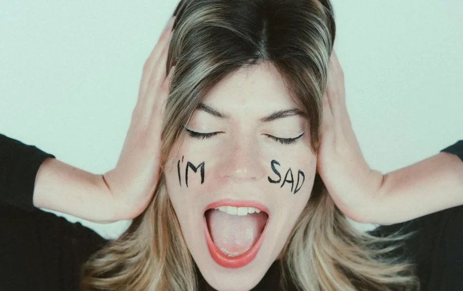 Woman acting as drama queen with hands over ears and words I'm Sad on her face
