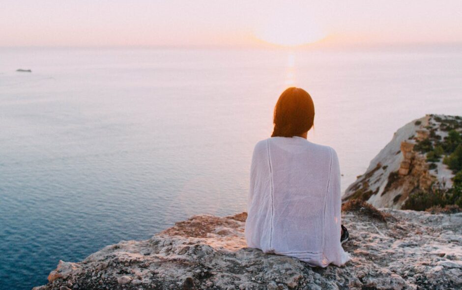 Intuition - woman sitting on rock looking at setting sun.