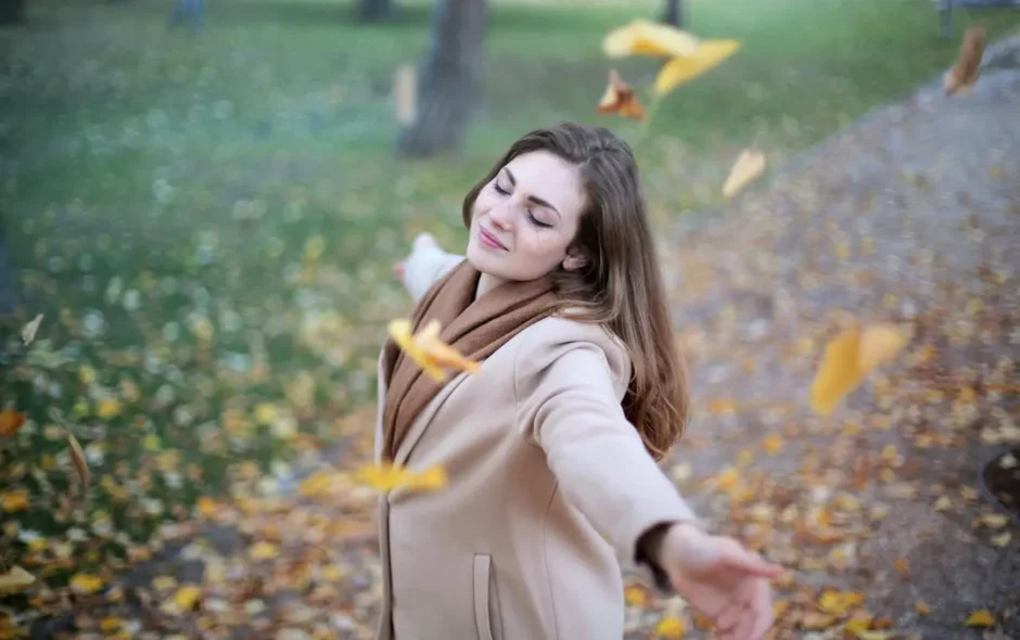 Woman in a park, eyes closed, arms outstretched, letting go of leaves.