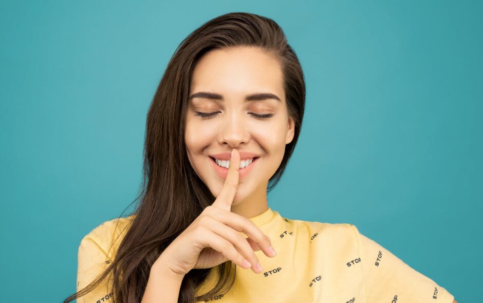 Woman with eyes closed and finger over her mouth quietening her voice