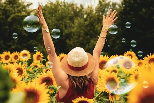 Woman in field of sunflowers embracing happiness with arms in air and bubbles all around